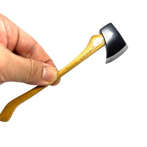 May include: A small axe featuring a wooden handle and a black metal blade. The handle is light brown, and the axe head is silver and black. The axe is set against a white backdrop.