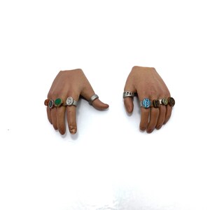Puede incluir: Dos manos con m&uacute;ltiples anillos en cada dedo. Los anillos son de plata con piedras de diferentes colores, incluyendo verde, azul, naranja y marr&oacute;n.