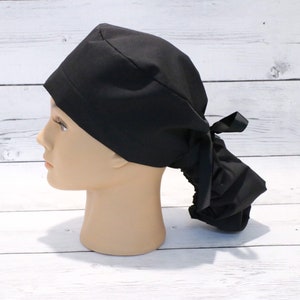 May include: A black scrub hat with a ponytail opening and a tie at the back.
