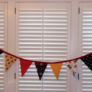 May include: A red, yellow, and black fabric banner with a Mickey Mouse theme. The banner is made of triangular flags with different patterns, including polka dots, stripes, and Mickey Mouse characters.