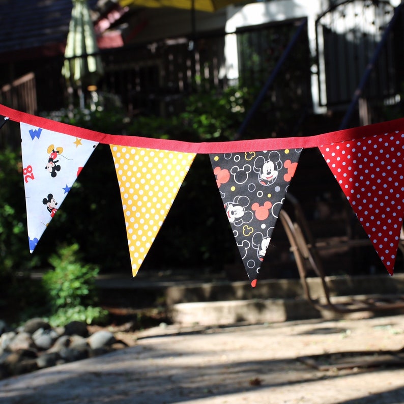 May include: A string of five triangular flags with a Mickey Mouse theme. The flags are red, yellow, black, and white with polka dots and Mickey Mouse images.