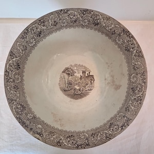 Könnte beinhalten: Große, runde, antike weiße Keramikschale mit braunem Blumenrand und einer zentralen Sepia-Landschaftsszene. Das Innere der Schale weist Gebrauchsspuren auf, was ihren Vintage-Charme unterstreicht.