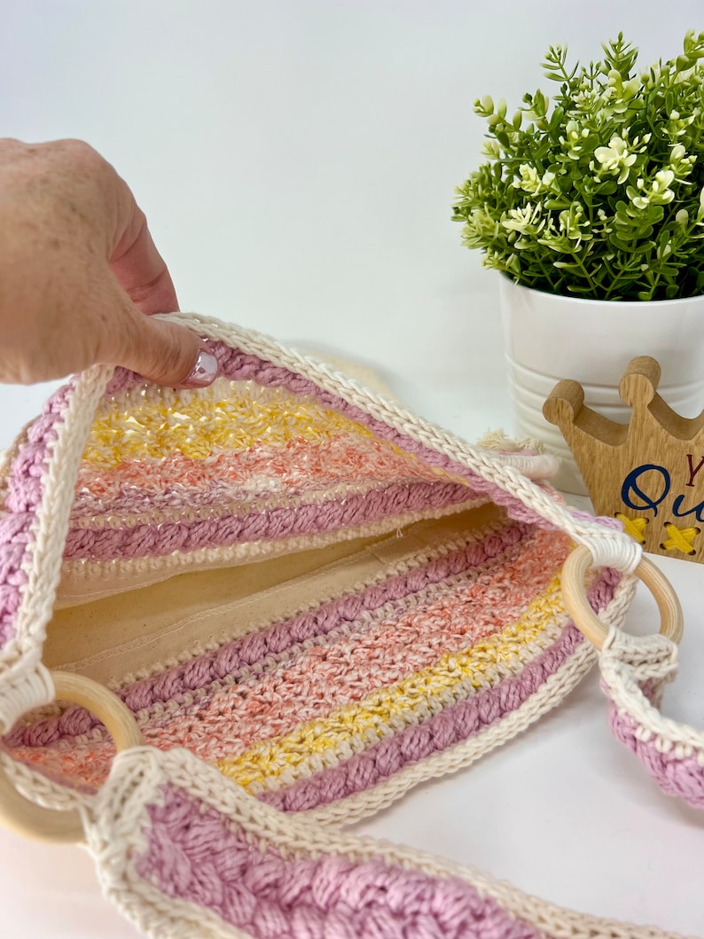 May include: A pink, yellow and white striped crochet tote bag with wooden handles. The bag is lined with a white fabric.