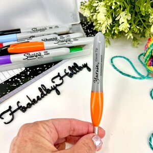 Pu&ograve; includere: Un uncinetto argentato e arancione con una punta argentata e il testo "Yarnie Clover Tip Permanent Maker" stampato sul lato.