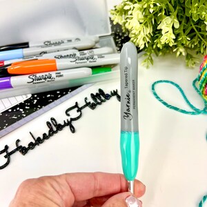 Pu&ograve; includere: Un uncinetto color turchese e grigio con una punta affusolata. L'uncinetto &egrave; etichettato "Yarnie Tapered Tip" e "Permanent Maker".