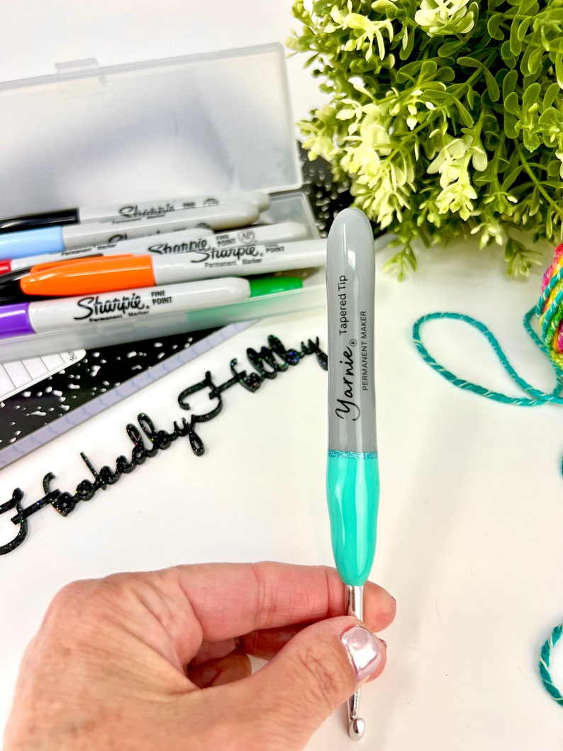 Pu&ograve; includere: Un uncinetto color turchese e grigio con una punta affusolata. L'uncinetto &egrave; etichettato "Yarnie Tapered Tip" e "Permanent Maker".
