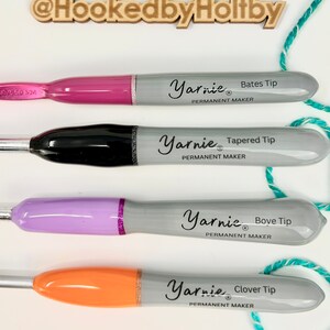 Pu&ograve; includere: Quattro pennarelli permanenti con punte di colore diverso e il testo "Yarnie&reg; Permanent Maker" sul lato. Le punte sono etichettate "Bates Tip", "Tapered Tip", "Bove Tip" e "Clover Tip".