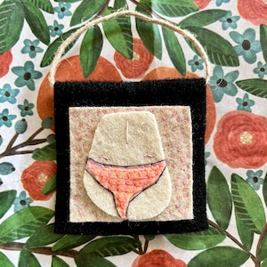 May include: A felt wall hanging with a pink and orange checkered pattern. The pattern is in the shape of underwear.