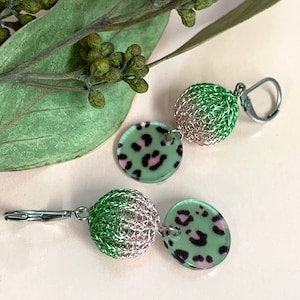 May include: Green and pink leopard print earrings with a silver wire mesh ball dangle. The earrings have a clip-on closure.