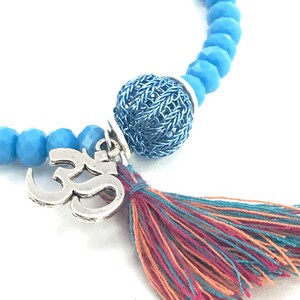 May include: A blue beaded bracelet with a silver Om charm, a blue wire ball, and a multi-colored tassel.