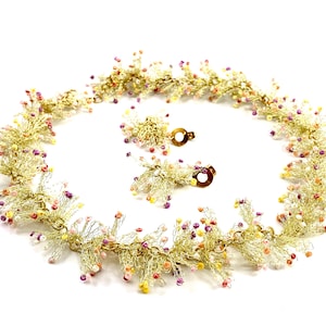 May include: A gold necklace and matching earrings with a delicate, lacy design. The necklace and earrings are adorned with small, colorful beads in shades of pink, yellow, and orange.