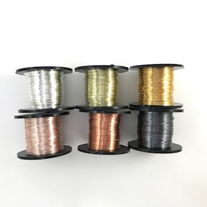 May include: Six spools of wire in different colors, including silver, gold, copper, and black. The spools are all the same size and are arranged in a row.