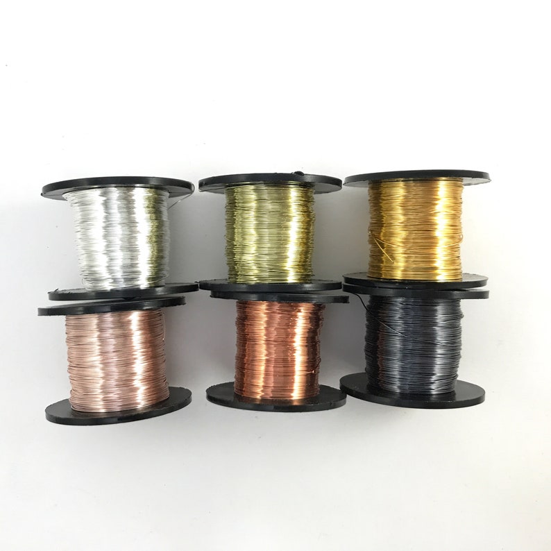 May include: Six spools of wire in different colors, including silver, gold, copper, and black. The spools are all the same size and are arranged in a row.