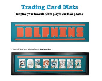 May include: A teal blue and orange trading card mat with the word "DOLPHINS" printed in large orange letters. The mat is framed in black and has a black background. The mat is designed to hold trading cards or photos.