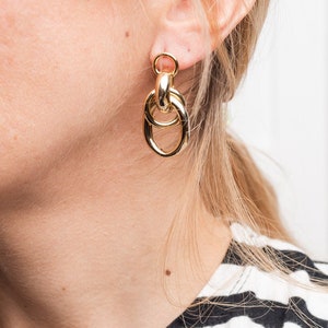 Peut inclure: Boucles d'oreilles créoles dorées avec un design noué. Les boucles d'oreilles sont pendantes et ont une finition polie.