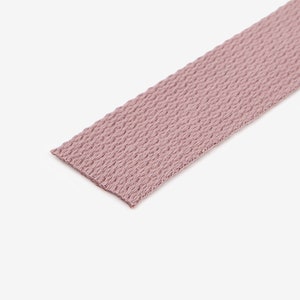 May include: A close-up of a light pink woven webbing strap.