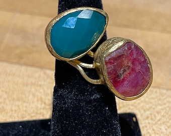 Könnte beinhalten: Ein goldener Ring mit zwei Edelsteineinsätzen. Der größere Stein ist tiefrosa, während der kleinere Stein blaugrün ist.