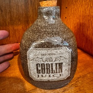 May include: A brown ceramic bottle with a cork stopper and a white label that reads "Goblin Juice".