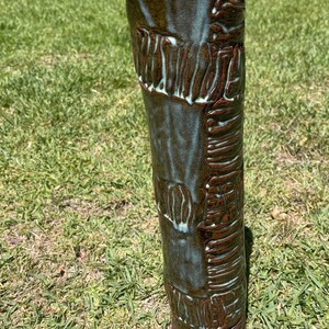 May include: A tall, cylindrical ceramic vase with a textured, brown and green glaze. The vase has a unique, organic shape and a rustic, handmade look.