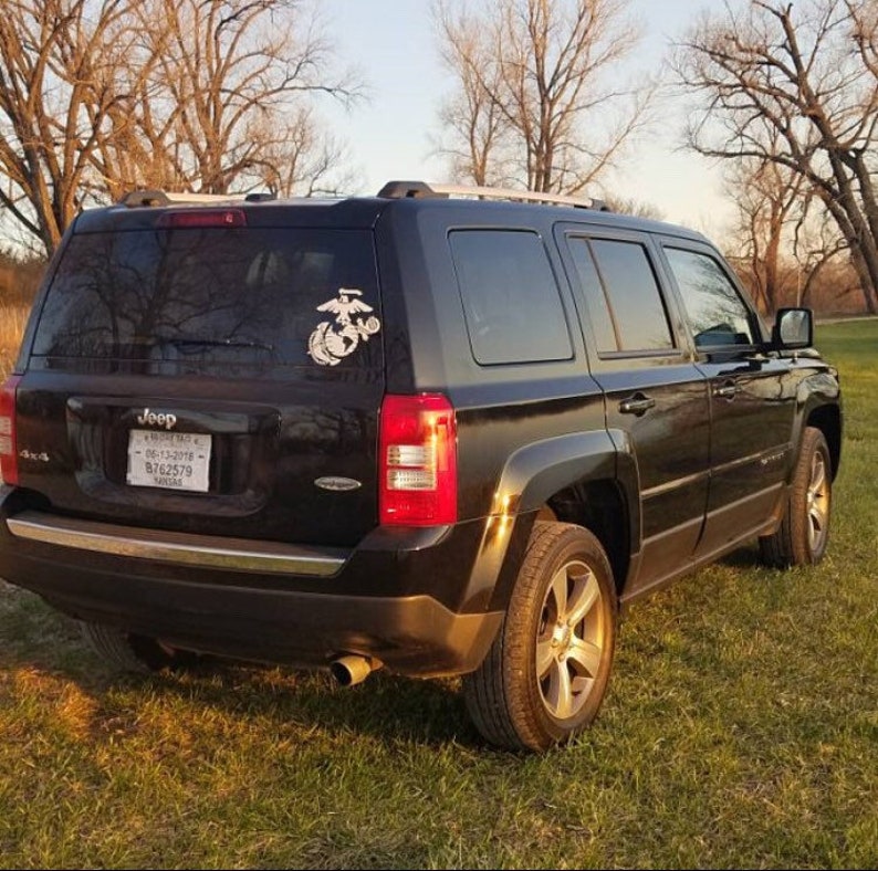 Puede incluir: Un Jeep Patriot negro con una baca de techo plateada y una pegatina con el emblema del Cuerpo de Marines de los Estados Unidos en la ventana trasera. La matr&iacute;cula dice "BG62579".