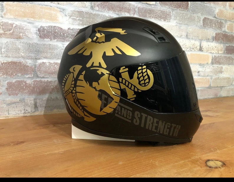 May include: Black motorcycle helmet with a gold eagle, globe, and anchor graphic. The helmet has a dark tinted visor and the text "SEMPER FIDELIS AND STRENGTH" is printed on the side.