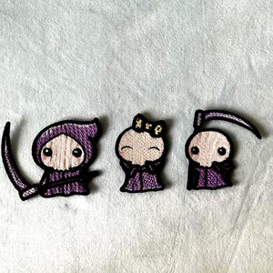 Puede incluir: Cinco parches bordados que muestran personajes estilizados con capas moradas con capucha, rostros pálidos y grandes ojos negros. Un personaje sostiene una guadaña, otro sostiene un pequeño objeto rojo y uno lleva un lazo amarillo.