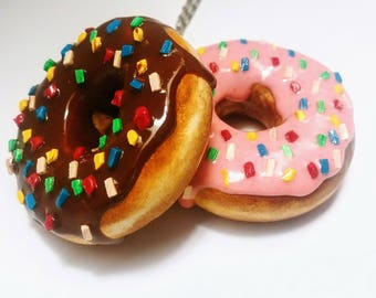 May include: Two mini donuts with colorful sprinkles. One donut is topped with chocolate frosting and the other with pink frosting.
