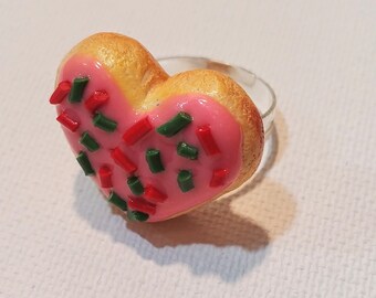 May include: A heart-shaped ring made of polymer clay, decorated with pink frosting and red and green sprinkles.
