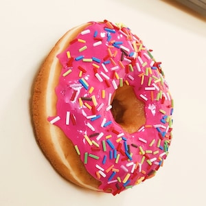 May include: A pink iced doughnut with colourful sprinkles.
