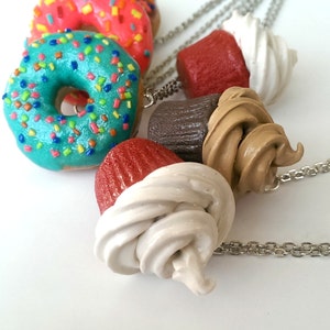 Puede incluir: Un conjunto de cinco amuletos de arcilla polim&eacute;rica de colores, que incluyen una dona azul con chispas de arco&iacute;ris, un cupcake rojo con glaseado blanco, un cupcake marr&oacute;n con glaseado marr&oacute;n, un cupcake rojo con glaseado blanco y un cupcake rojo con glaseado blanco. Los amuletos est&aacute;n unidos a cadenas plateadas.