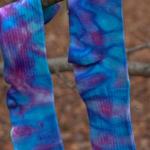 May include: Two pairs of tie-dye socks in shades of blue, purple, and pink hanging on a branch.