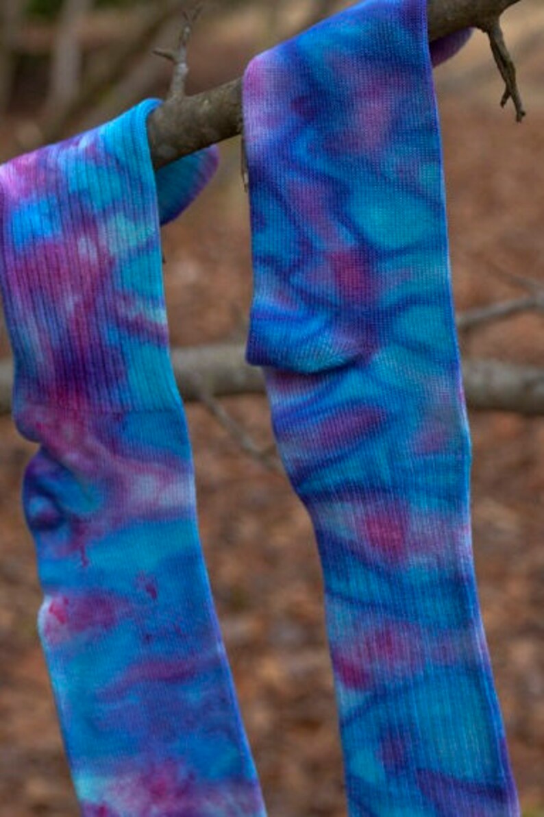 May include: Two pairs of tie-dye socks in shades of blue, purple, and pink hanging on a branch.