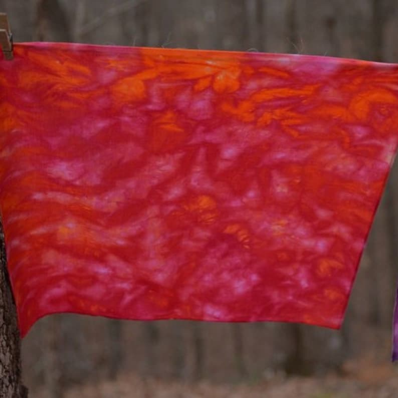 May include: A red and orange tie-dye fabric with a swirling pattern. The fabric is hanging on a clothesline.