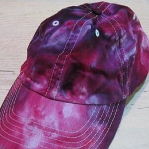 May include: A purple and pink tie-dye baseball cap with a white brim and eyelets.
