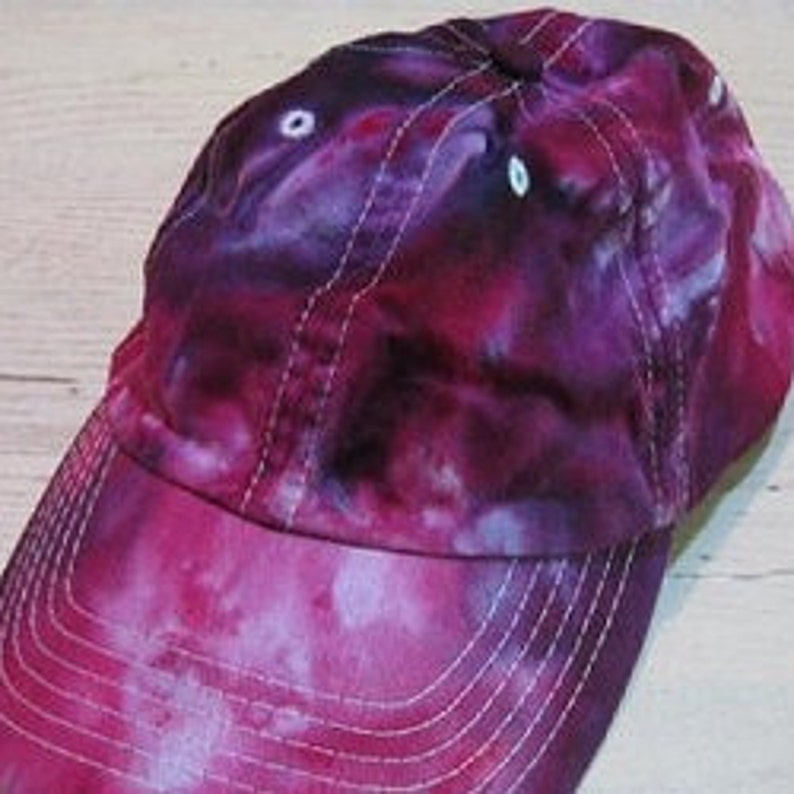 May include: A purple and pink tie-dye baseball cap with a white brim and eyelets.