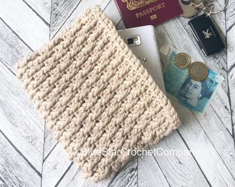 May include: A beige crocheted clutch purse with a zipper closure. The purse is open and contains a passport, a cell phone, keys, and British currency.