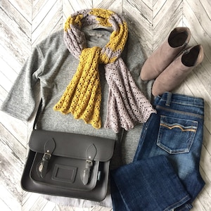 May include: A gray sweater, a yellow and purple crocheted scarf, a black leather satchel bag, blue jeans, and brown ankle boots.