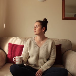 Woman wearing a beige, hand-crocheted V-neck sweater with black leggings