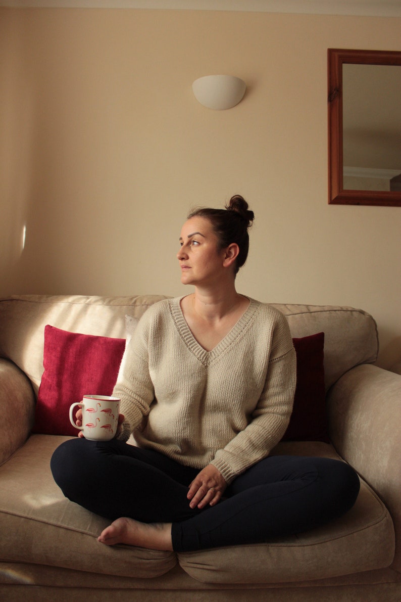 Woman wearing a beige, hand-crocheted V-neck sweater with black leggings