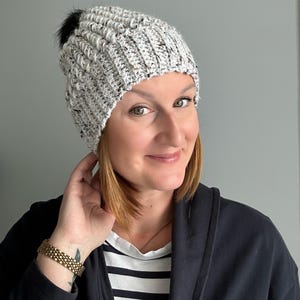 以下が含まれることがあります： 黒いポンポンが付いた、グレーと白のニット帽。 リブ編みのテクスチャで、まだら模様の糸で作られています。 寒い季節にぴったりの、おしゃれな冬のアクセサリーです。