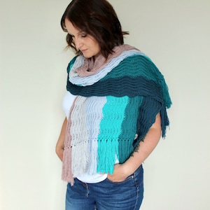 May include: A woman wearing a multi-colored crocheted shawl with fringe. The shawl is made in shades of pink, blue, teal, and green.
