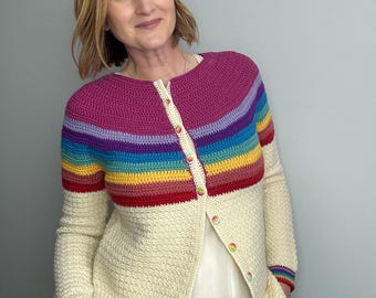 Può includere: Un cardigan all'uncinetto color crema con carrè e polsini a righe arcobaleno. Il cardigan ha un motivo a punto strutturato e si abbottona sul davanti con bottoni colorati. Le maniche sono lunghe e lo stile generale è casual.