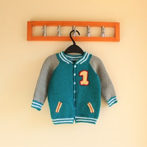 May include: Teal and gray knitted varsity jacket with white stripes and the number "1" on the front. The jacket has a button-up closure and two small pockets. The jacket is hanging on a black hanger.