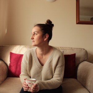 Woman wearing a beige, hand-crocheted V-neck sweater with black leggings