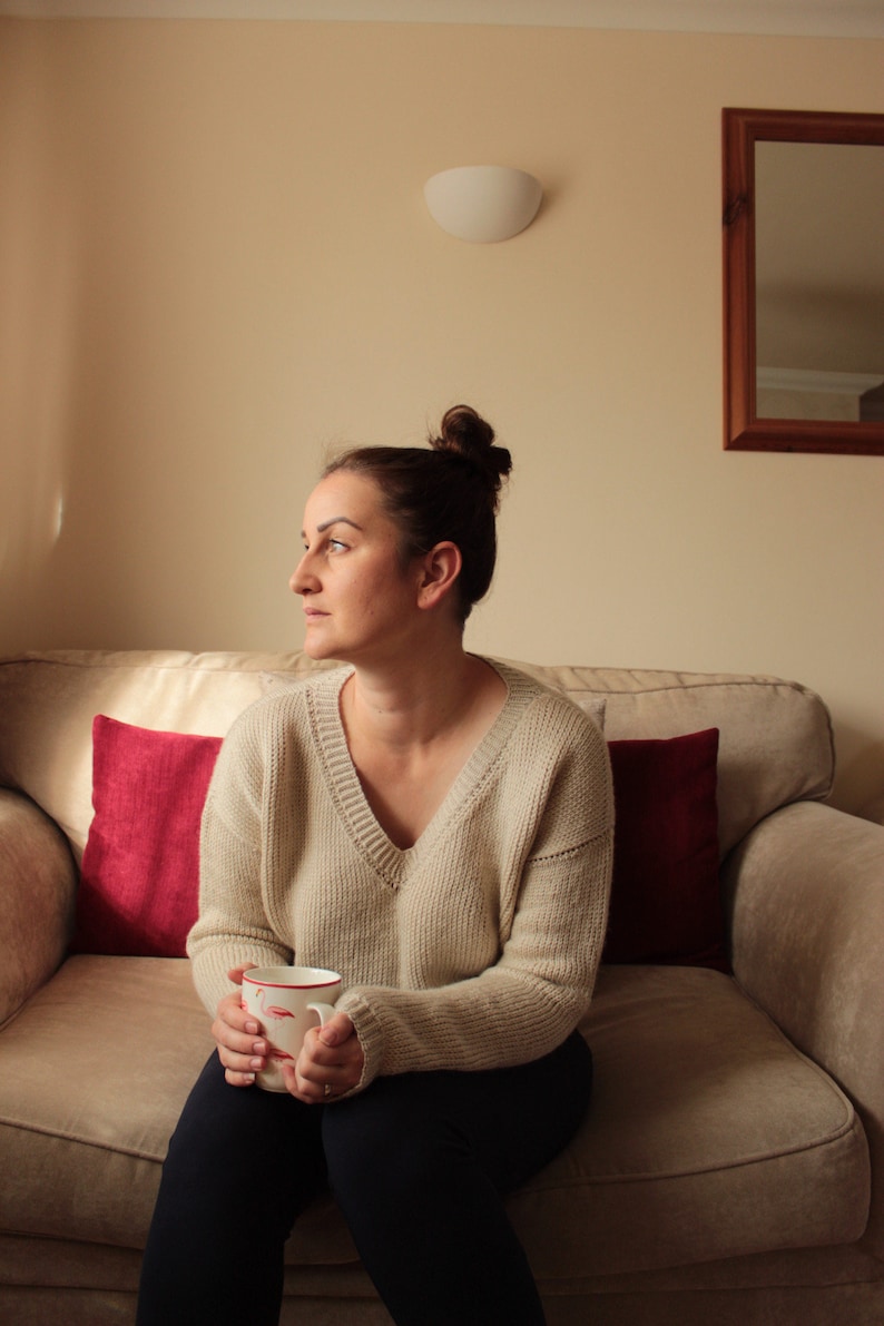 Woman wearing a beige, hand-crocheted V-neck sweater with black leggings