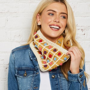 May include: A crocheted cowl with a geometric pattern in shades of yellow, white, red, blue, and purple. The cowl has a textured, waffle-like design and is accented with small, colourful bobbles.
