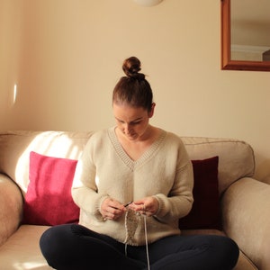 Woman wearing a beige, hand-crocheted V-neck sweater with black leggings