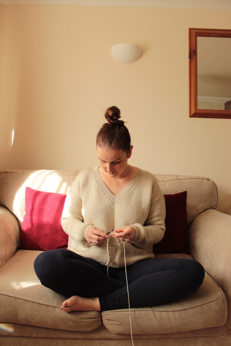 Woman wearing a beige, hand-crocheted V-neck sweater with black leggings
