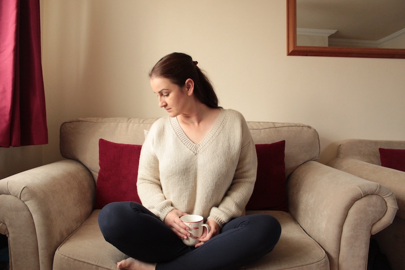Woman wearing a beige, hand-crocheted V-neck sweater with black leggings