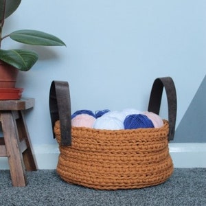 May include: A brown crocheted basket with two dark brown leather handles filled with colorful yarn balls.